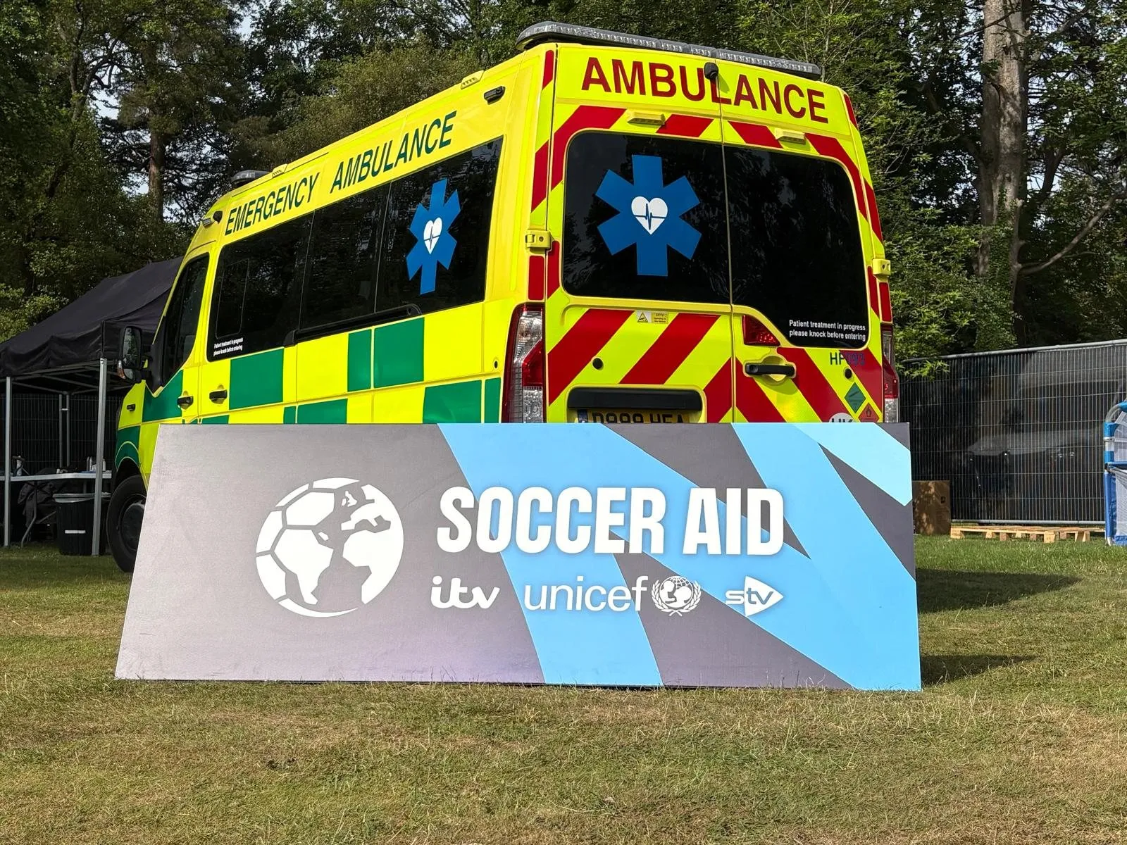 A Hearts First ambulance parked beside a Soccer Aid sign at an event