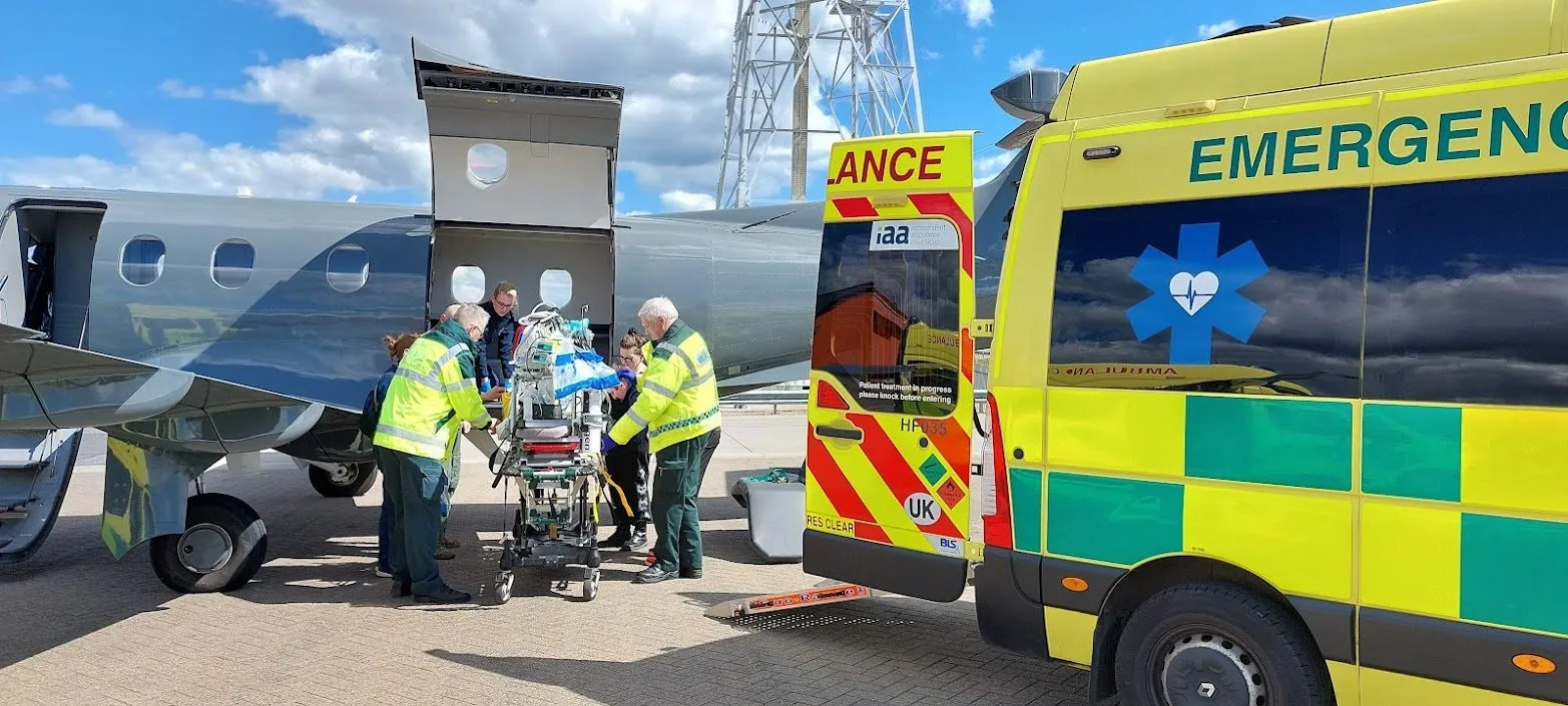 Crew transferring a patient on a stretcher between an ambulance and an aircraft on the airfield