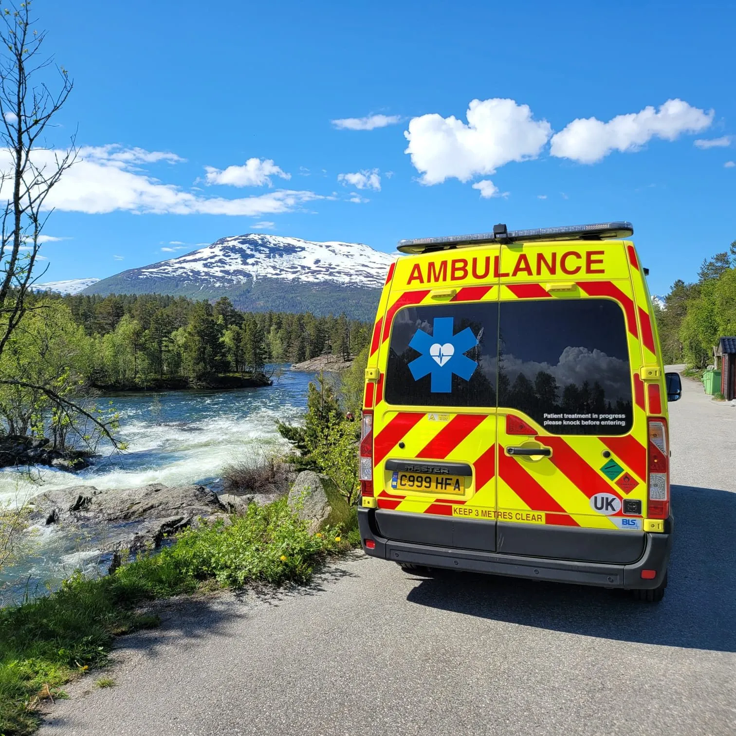 A Hearts First ambulance parked beside a river with a snow-capped mountain behind