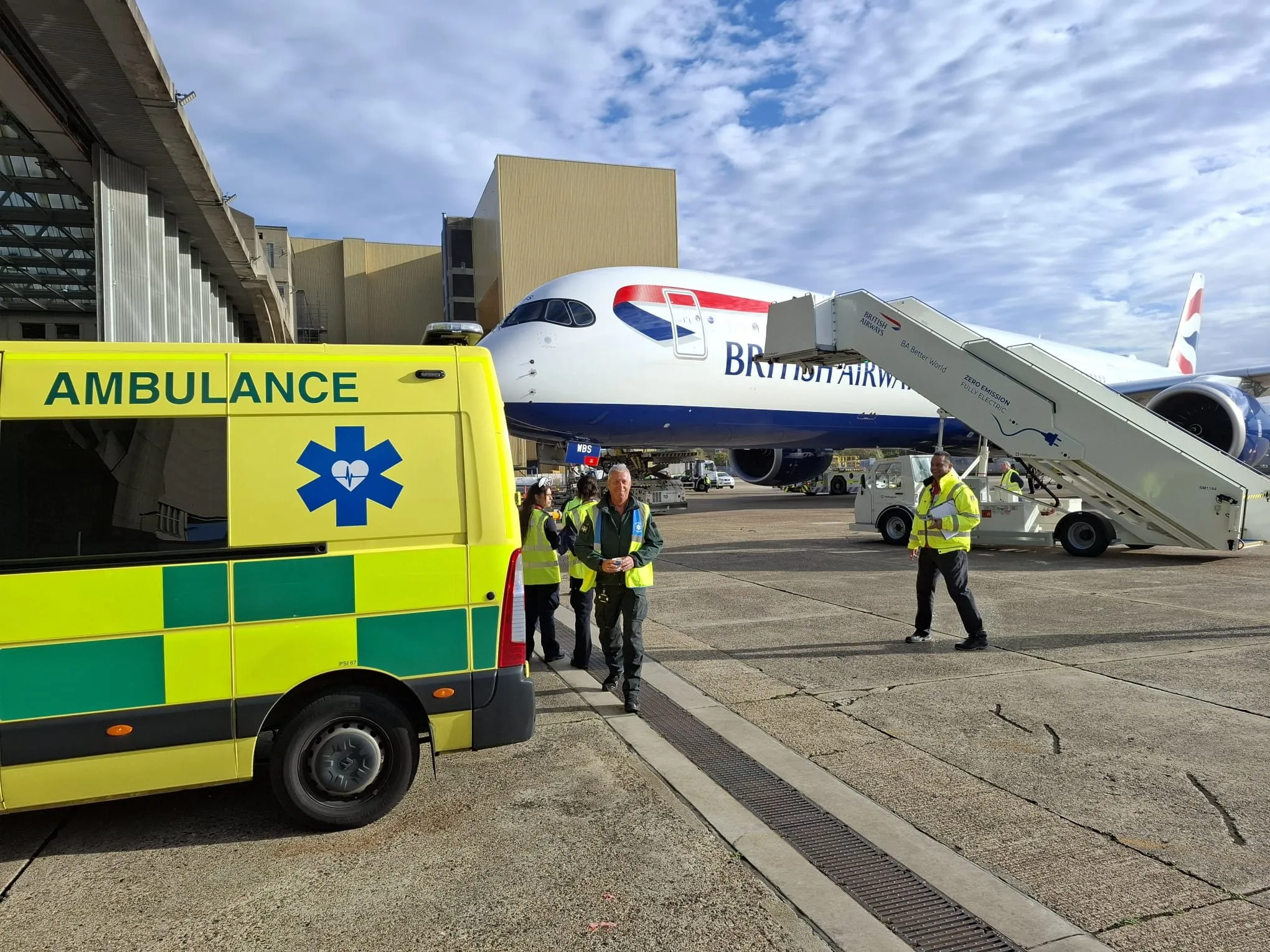 An ambulance and crew beside a passenger aircraft and boarding steps at an airport